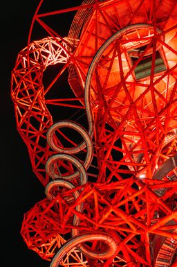 An external shot of the Helix slide at Zip World London, surrounded by a red metal structure lit-up in bright red lighting at night