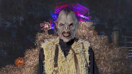 A noseless, snarling monster in a fur gilet stands before a stack of hay.