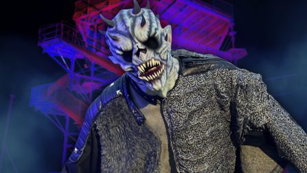 A blue-skinned creature with blackened eyes and horns growing out of its head stands angrily in front of an illuminated climbing frame structure.
