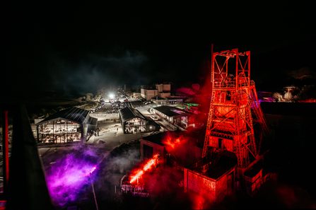 A birds-eye view of a scare-fest, featuring a big tower colliery structure lit in bright red lighting in the foreground